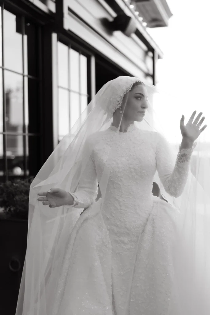 Black-and-white portrait of a bride in a veil beside a window