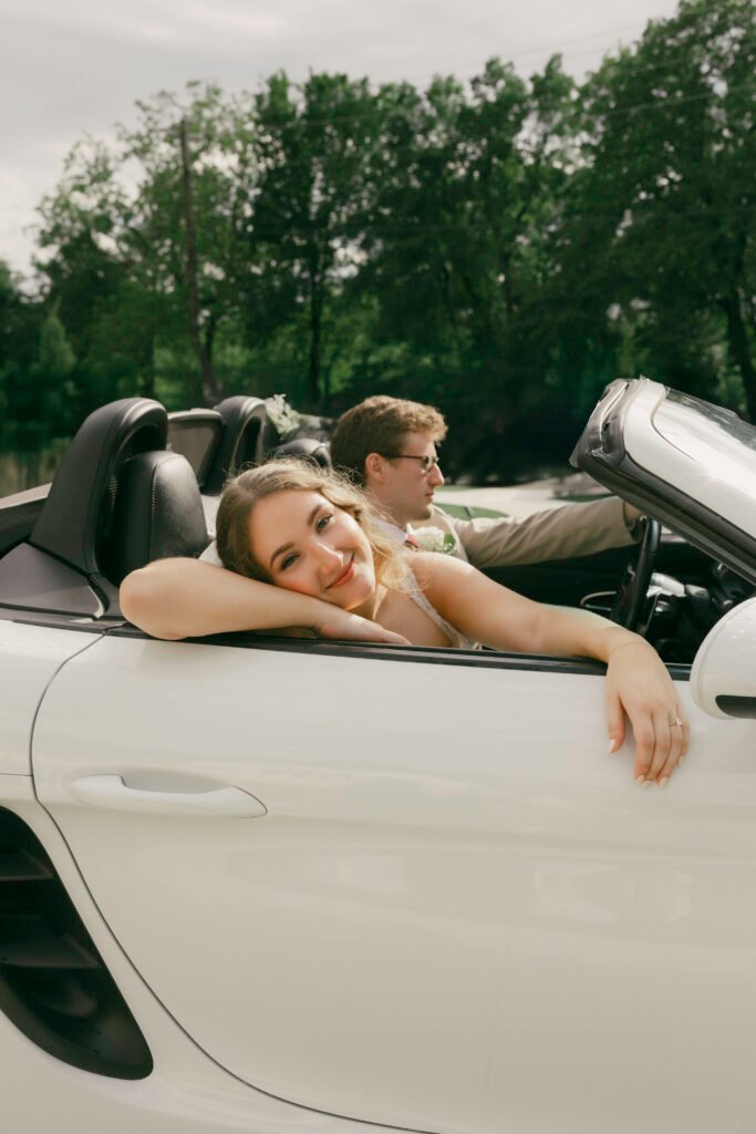 Bride leaning over the side of a white convertible with the groom seated beside her